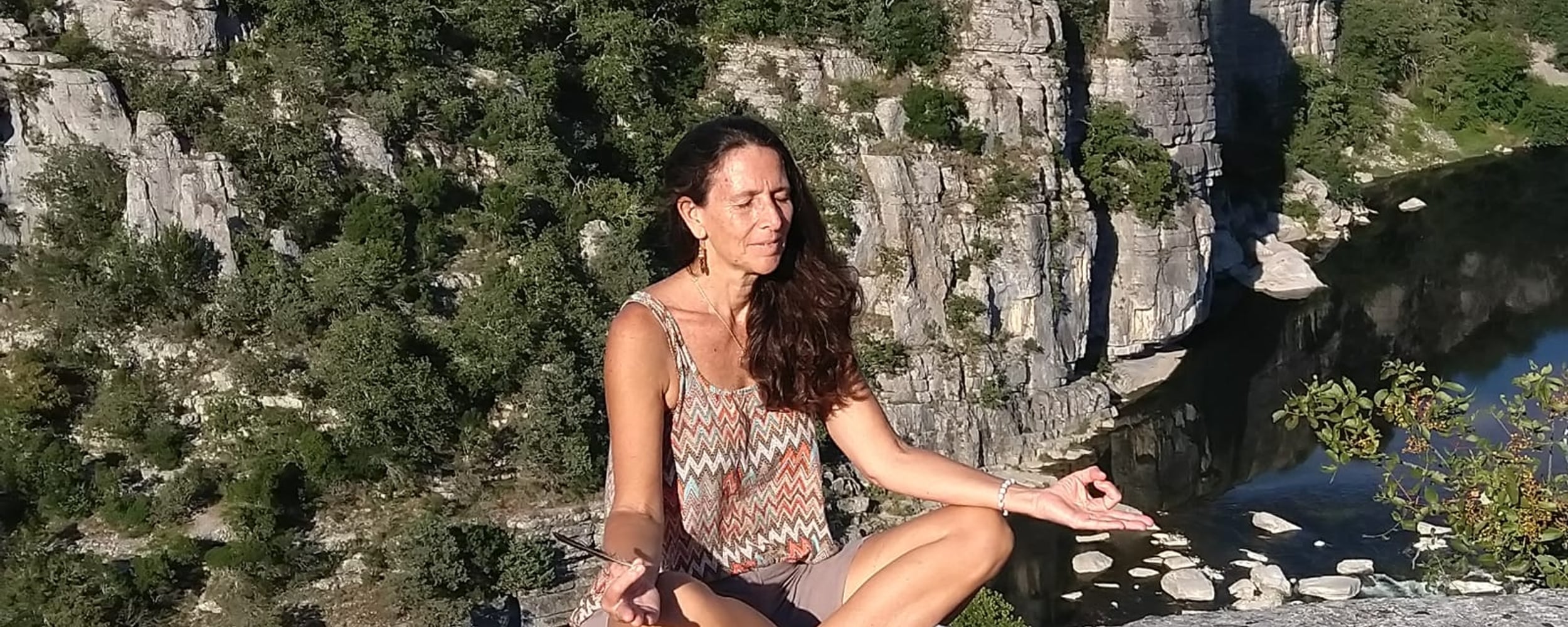 Femme en méditation assise sur un rocher face aux gorges cévenoles, les yeux fermés en connexion intérieure